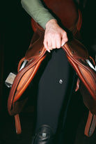 Person holding a brown leather saddle with a black background