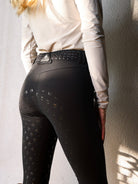 Person wearing black riding pants with a pattern on a plain background