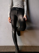 Person wearing black riding pants against a plain wall