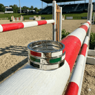 Silver ring with colored bands on a red and white striped barrier in an equestrian arena.