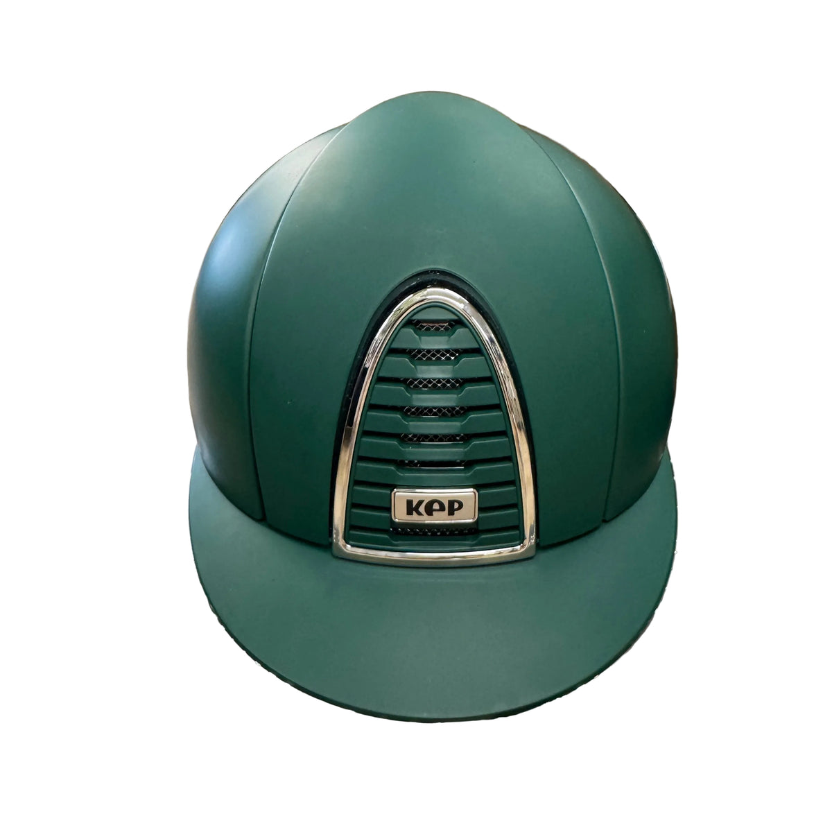 A dark green equestrian riding helmet with a silver-trimmed KPP front badge, resting on a patterned brown and white box in an indoor room setting.