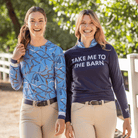Two women wearing equestrian-themed sweaters outdoors with trees in the background
