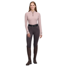 A woman modeling a light pink long-sleeve quarter-zip top, dark gray riding breeches, a black belt, and dark brown riding boots against a plain white background.