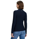 A woman shown from the back wearing a fitted navy long-sleeve mock-neck top and blue jeans against a light gray studio background.