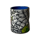 Ceramic tumbler with black and white leaf pattern and blue interior on a beige background