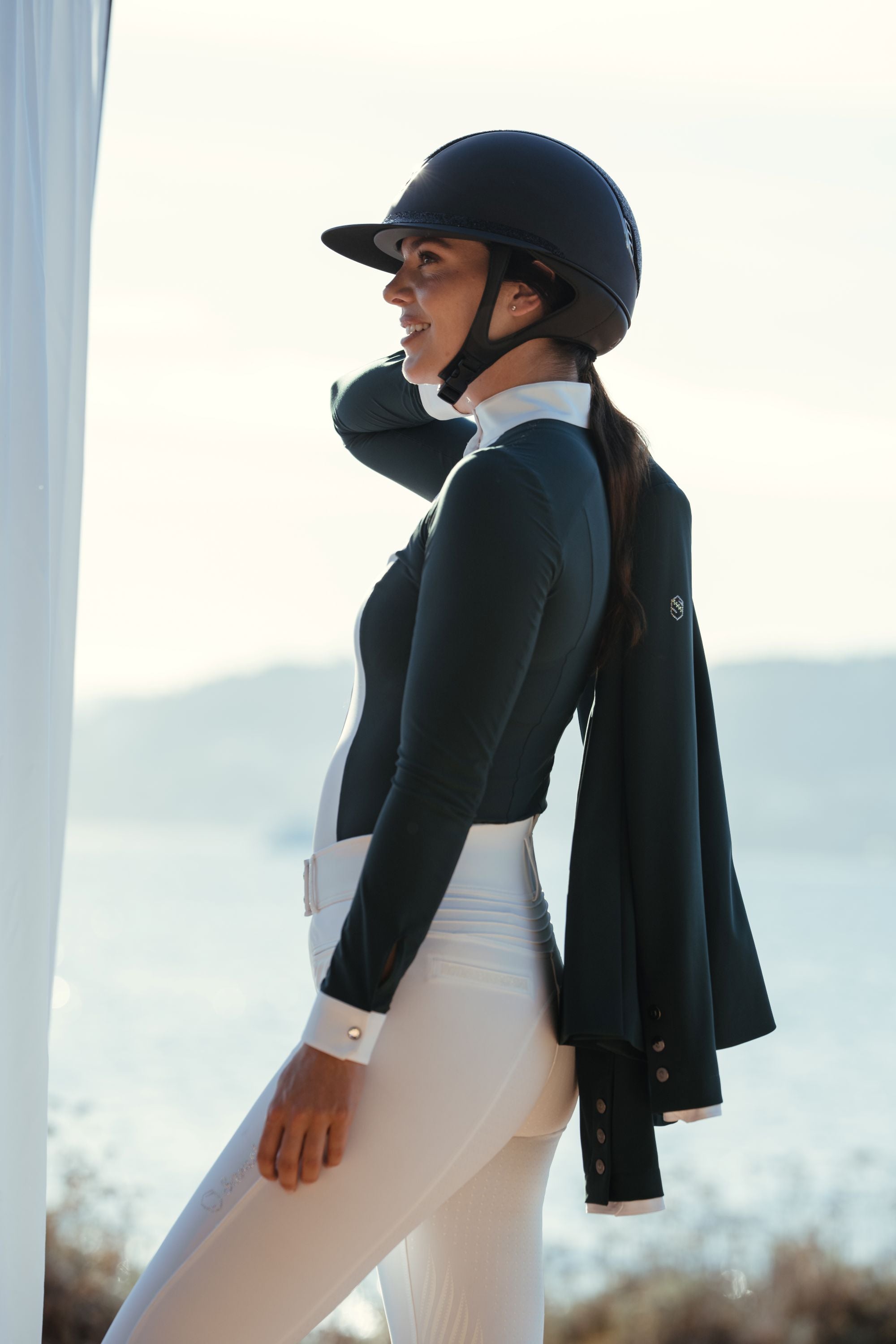 Woman in equestrian attire with a helmet and jacket outdoors