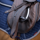 Brown leather saddle on a blue quilted saddle pad with visible brand name.