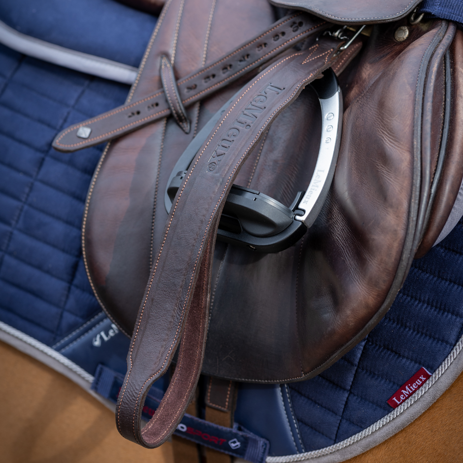 Brown leather saddle on a blue quilted saddle pad with visible brand name.