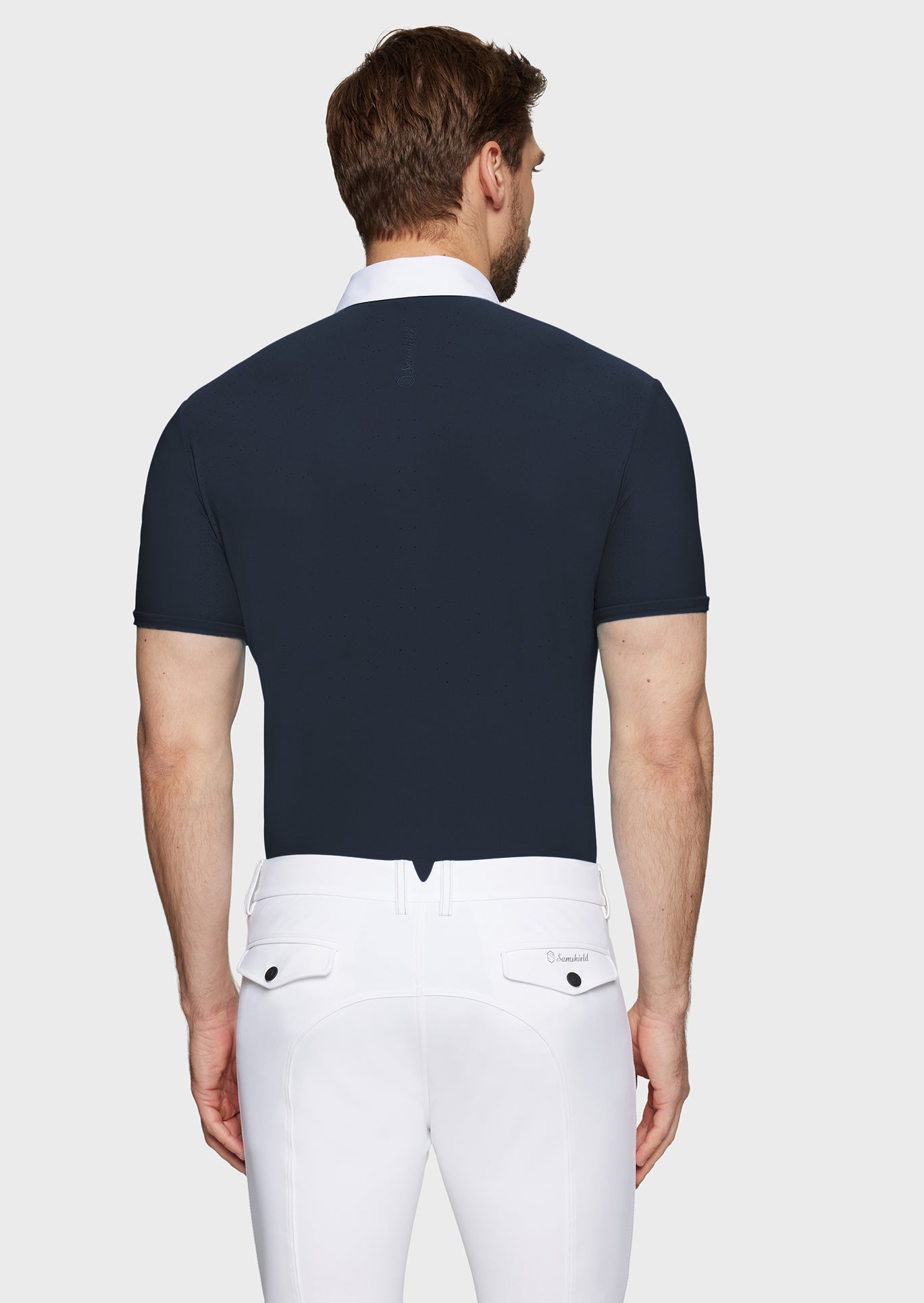 Man wearing a navy polo shirt and white pants on a light gray background