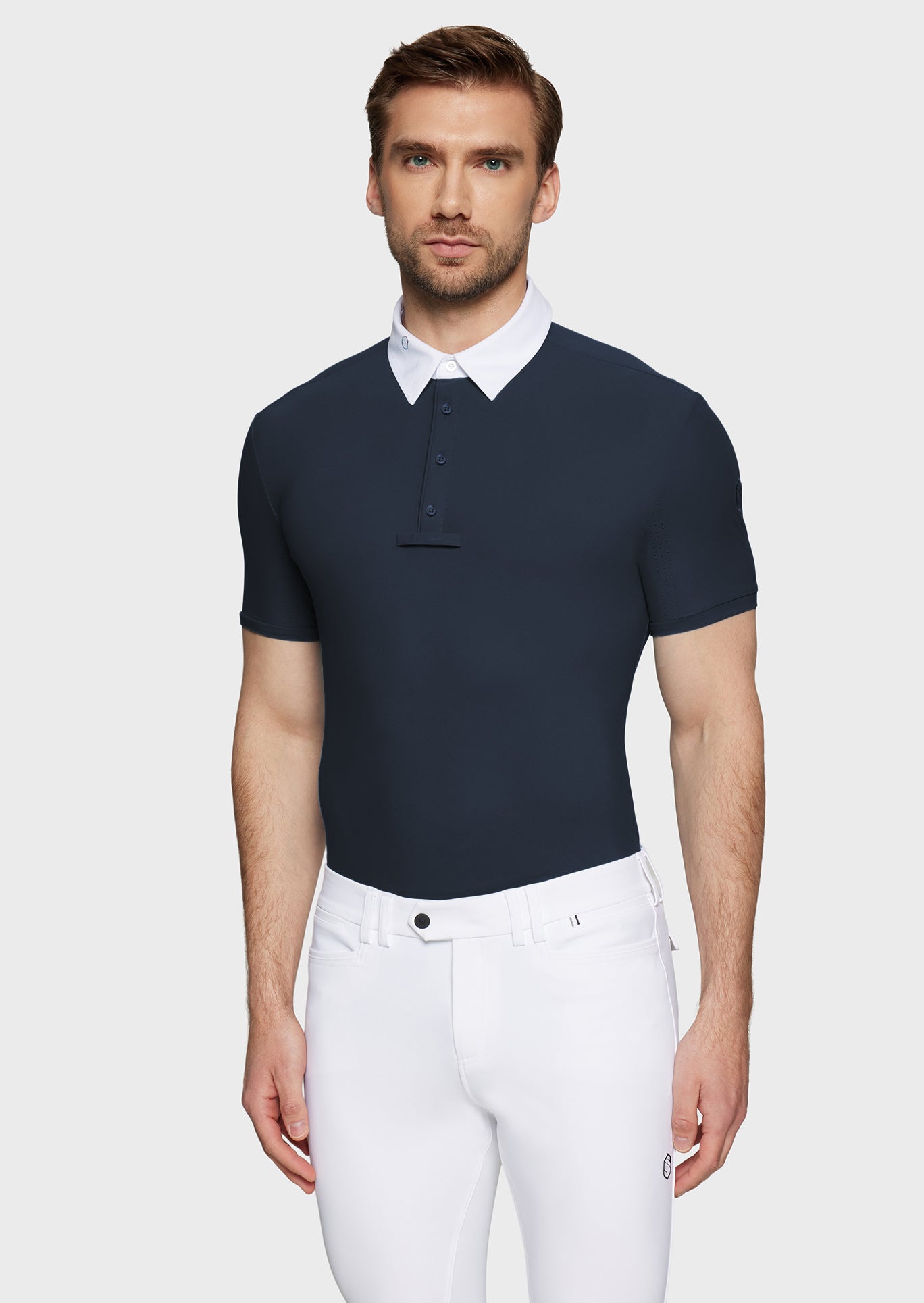 Man wearing a navy polo shirt with a white collar and white pants on a light gray background