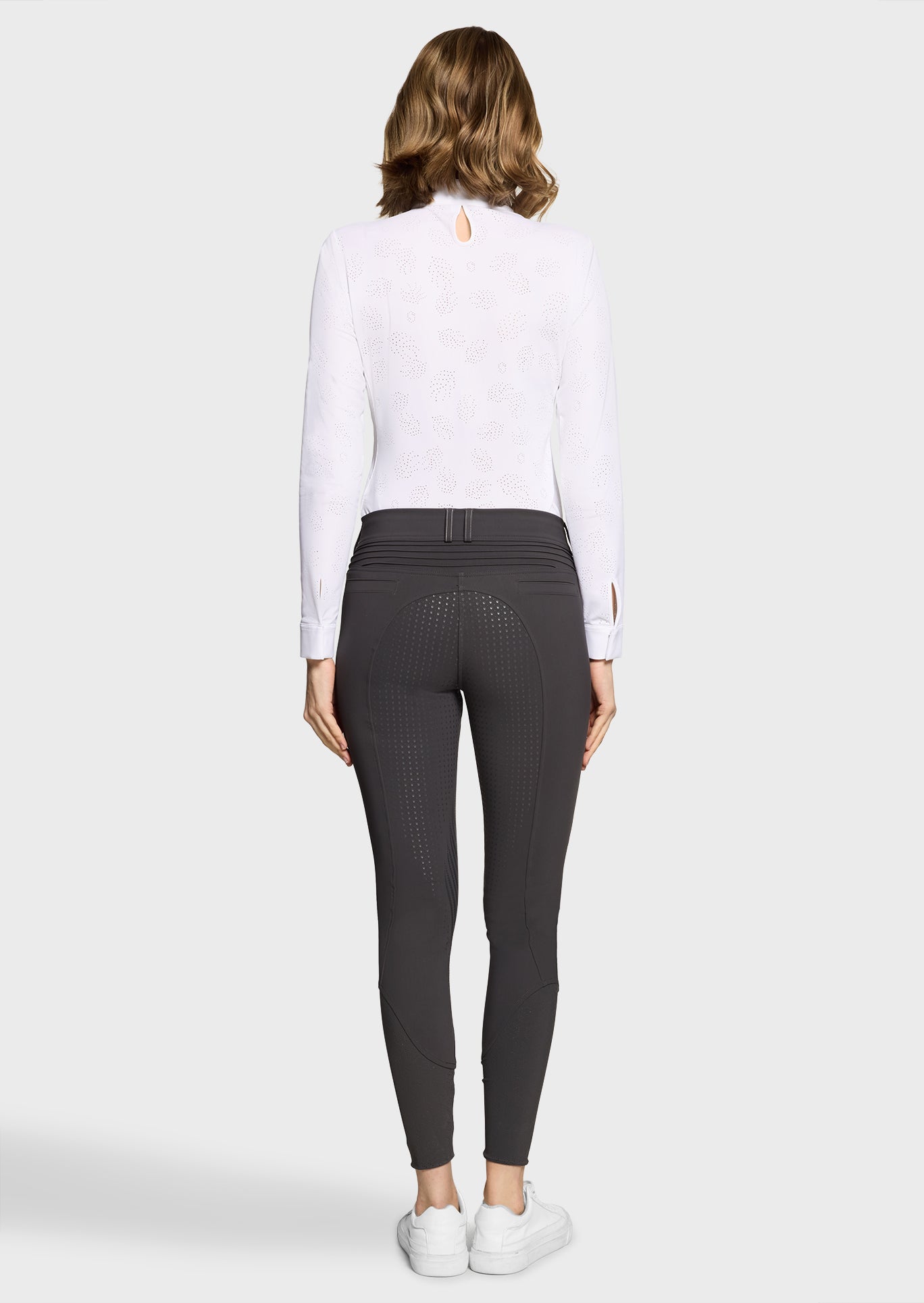 Woman wearing a white long-sleeve top and dark gray leggings on a white background