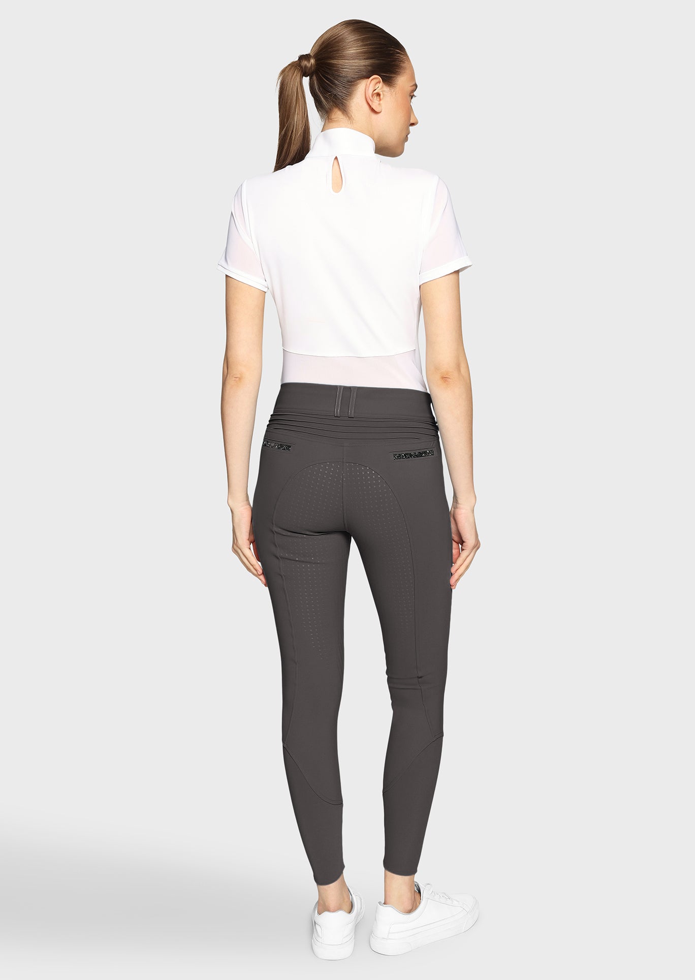 Woman wearing navy riding pants and a white shirt on a white background