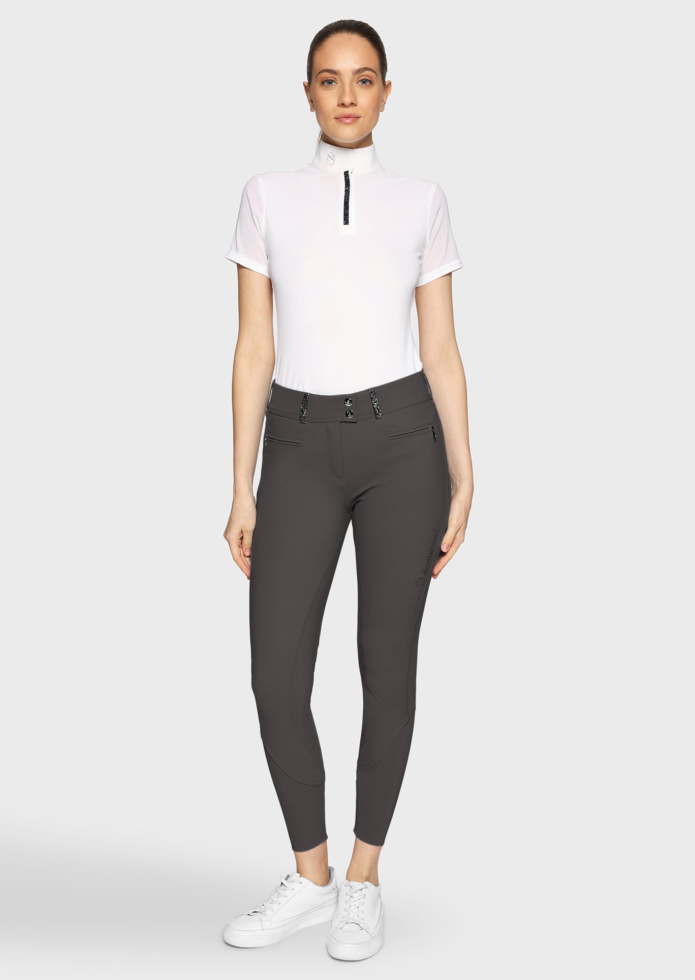 Woman wearing a white top and gray riding pants on a white background