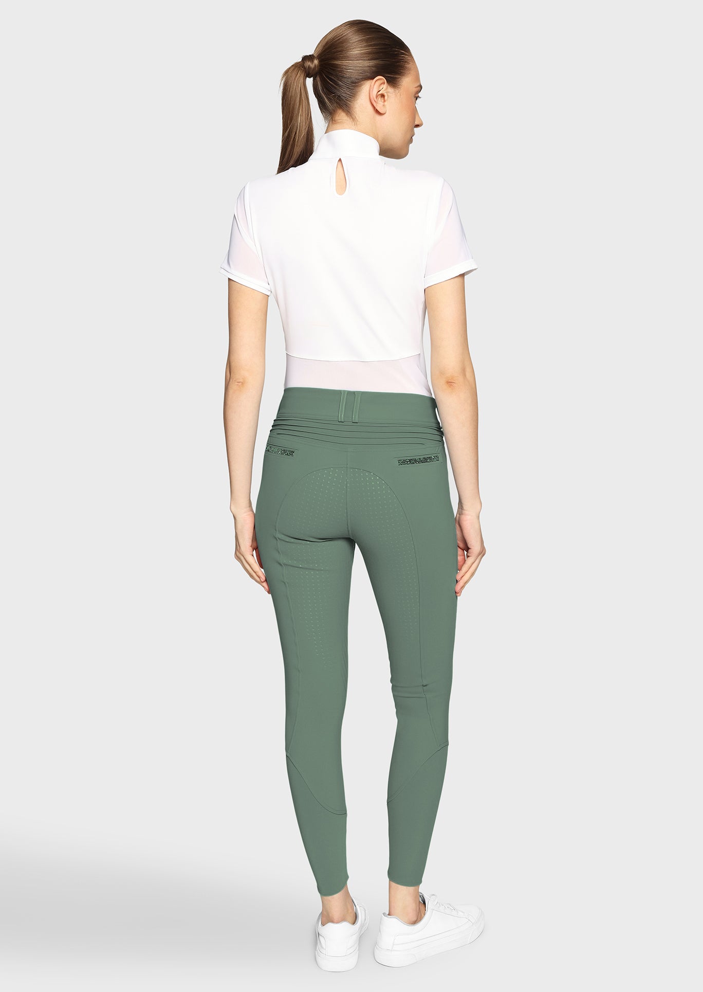 Woman wearing green pants and a white top on a light gray background