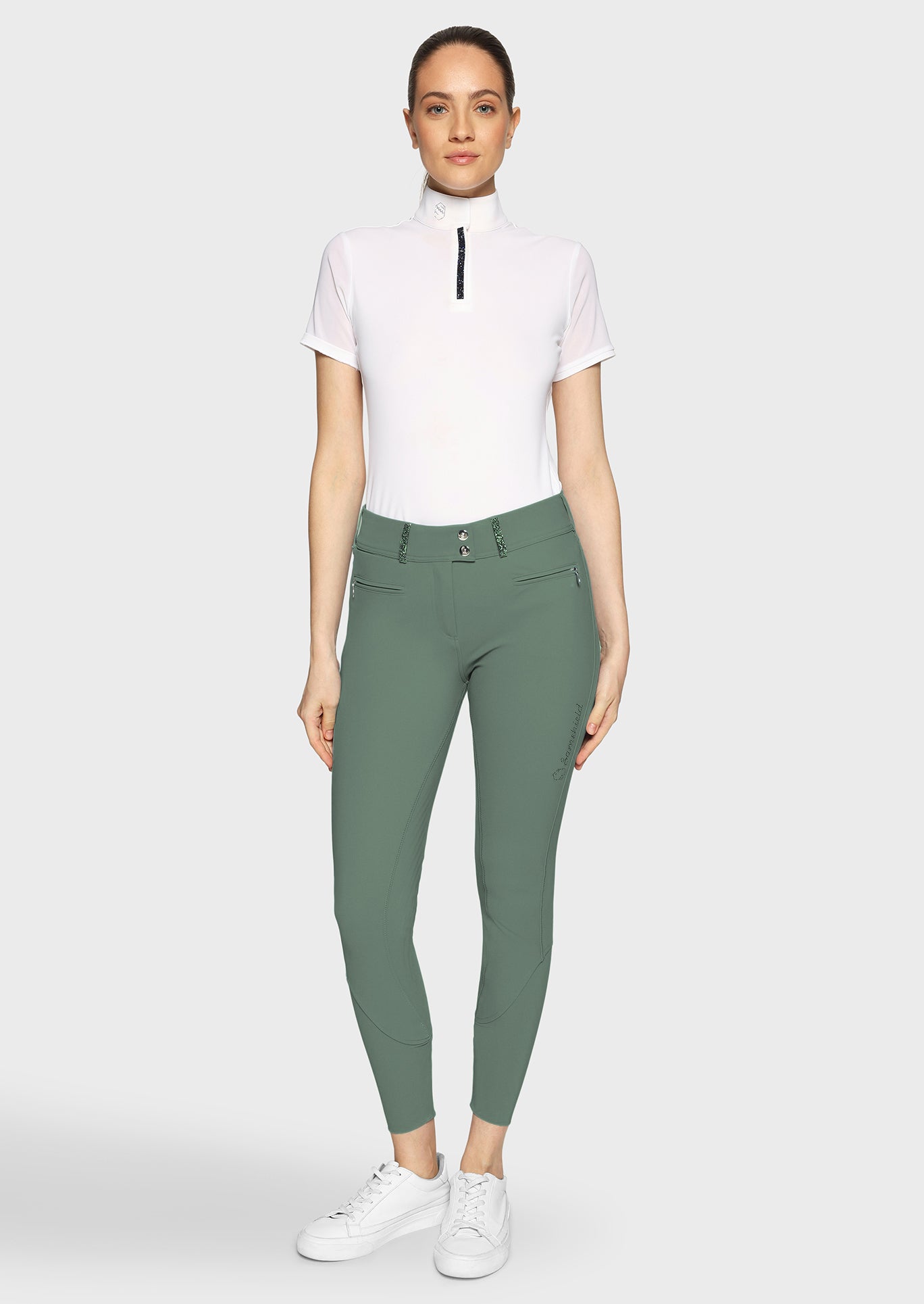 Woman wearing green riding pants and a white top on a white background