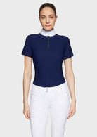 Woman wearing a navy blue top with a white collar and white pants on a light gray background