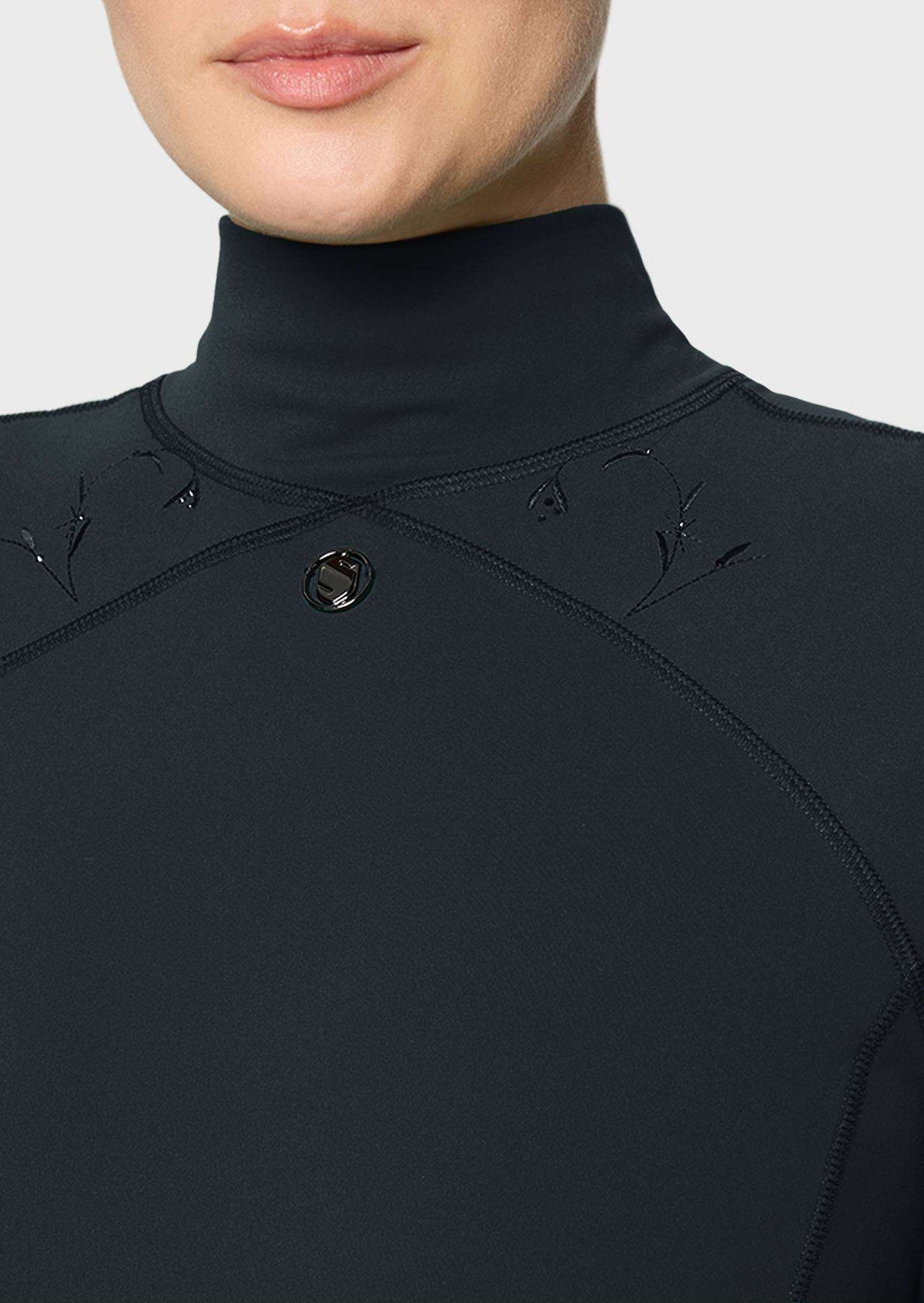 Close-up of a person wearing a black high-neck top with subtle embroidered leaf details on the shoulders and a small circular logo button at the center chest, against a light gray background.
