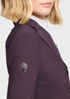 Close-up of a model wearing a dark plum purple blazer with decorative silver rhinestone embroidery on the shoulder and a matching embroidered shield patch on the sleeve, paired with a white collared shirt.