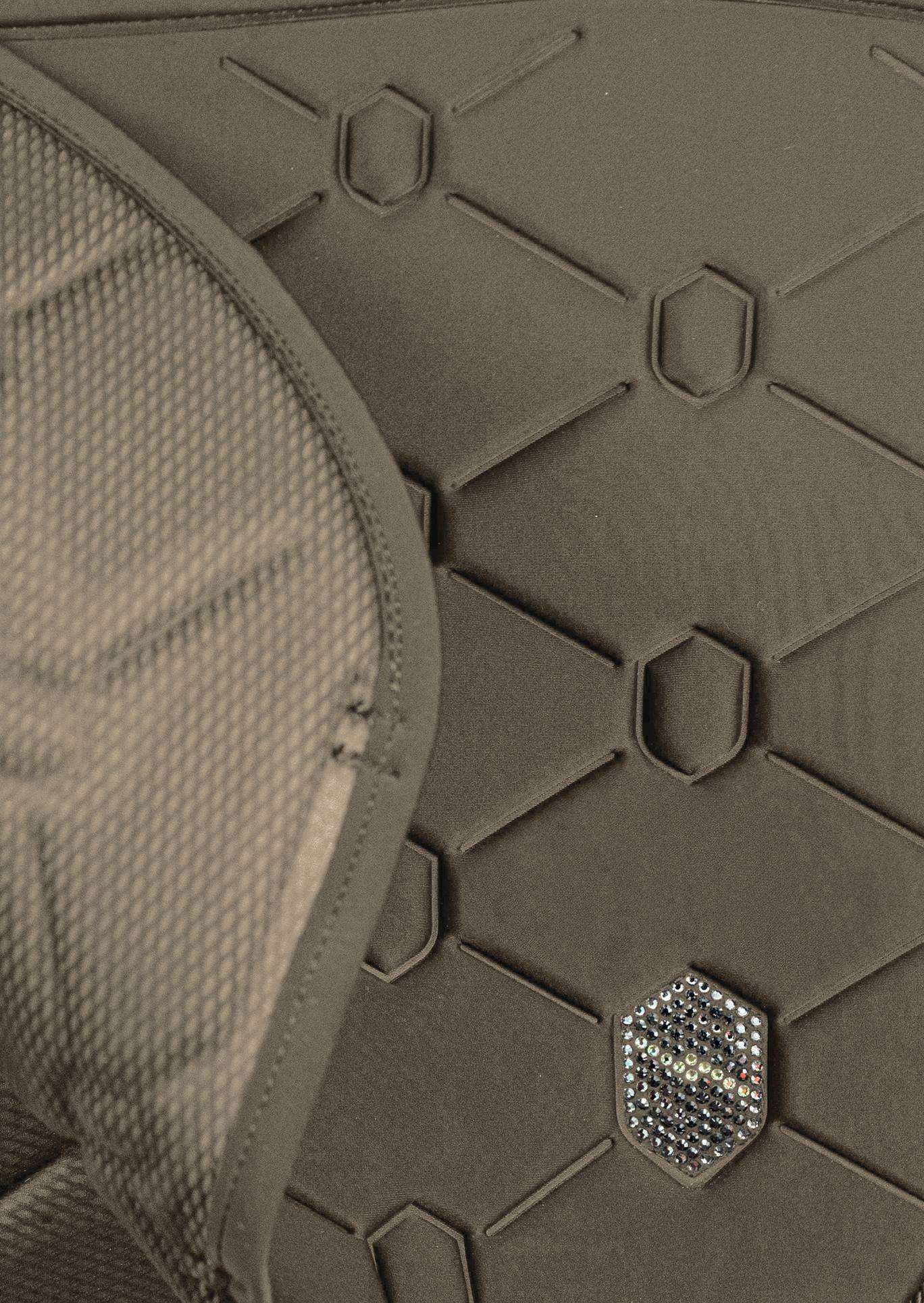 Close-up detail of a dark olive green protective pad or armor plate with a honeycomb pattern, featuring a small hexagonal metallic logo badge.