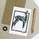 Greeting card with a dog illustration and 'Happy Birthday!' text, placed on a glittery surface with a pen and envelope.