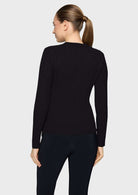 A woman shown from the back wearing a black cable-knit long-sleeve sweater and black leggings against a light gray studio background.