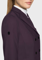 A close-up side view of a model wearing a dark plum purple double-breasted blazer over a white collared shirt, set against a plain light gray background.