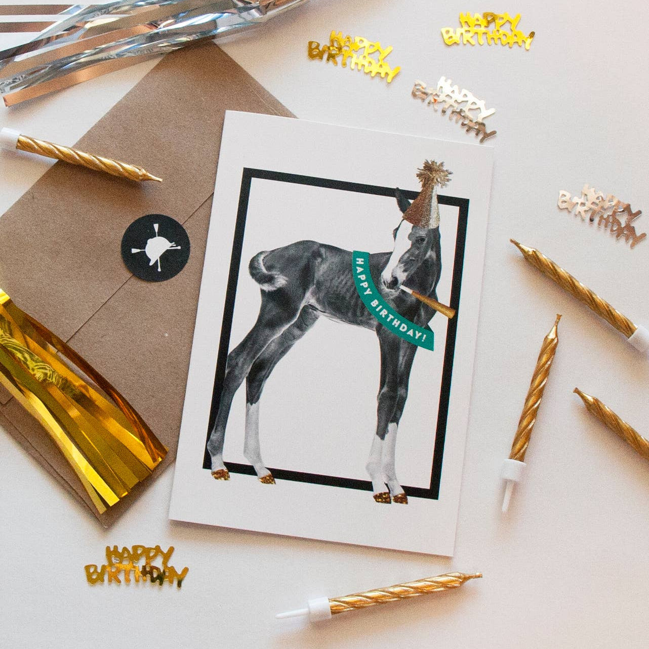 Birthday card with a foal illustration surrounded by birthday candles and confetti on a light background