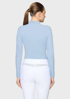 A woman shown from the back wearing a light blue long-sleeve mock-neck riding crop top and white riding breeches with a decorative silver floral waistband.