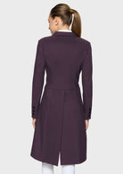 A woman viewed from the back wearing a dark plum purple tailored coat over a white collared shirt and white pants, against a light gray studio background.