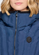 Close-up of a person wearing a navy blue puffer jacket with a black zipper, black collar, and a black hexagonal logo patch on the chest.