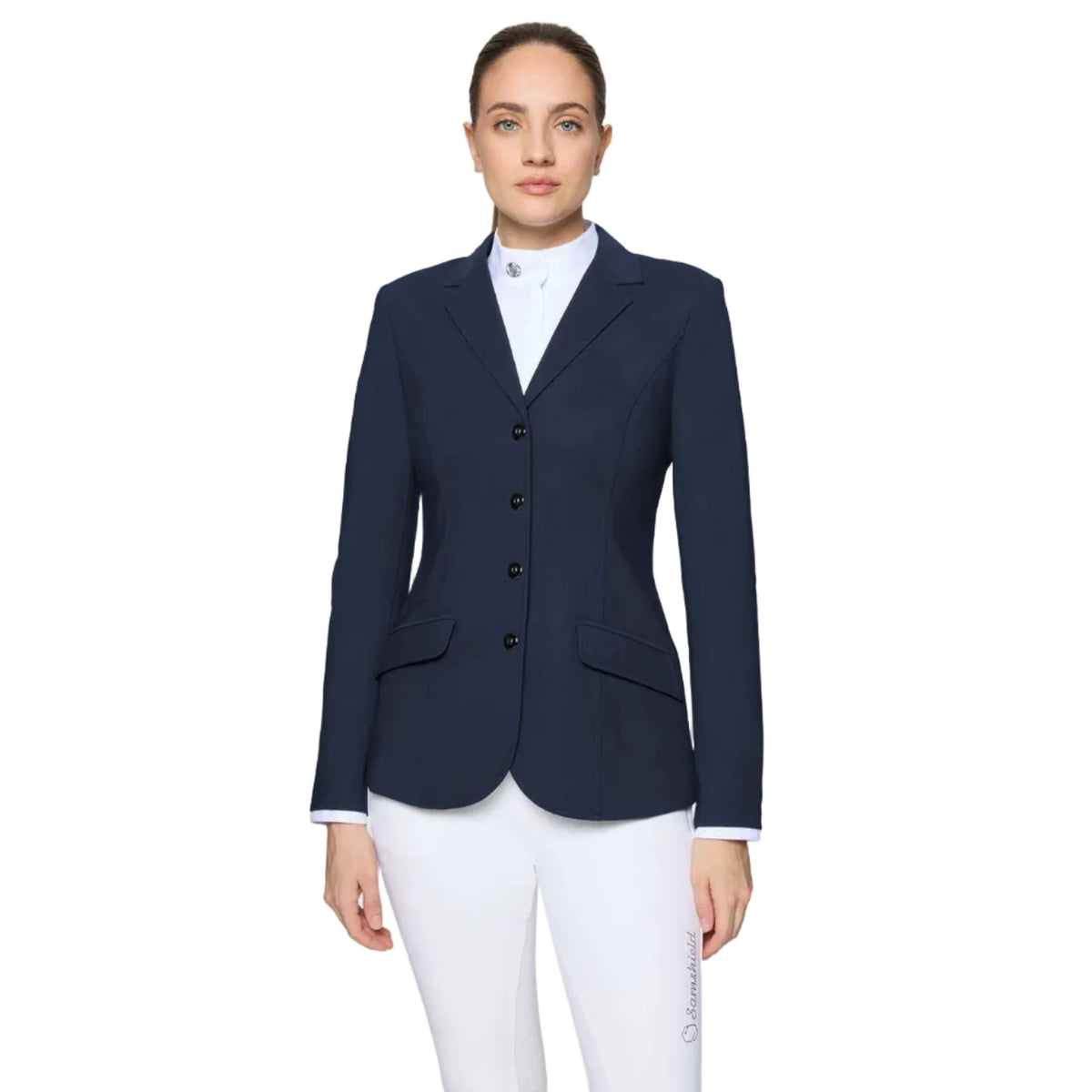 A woman modeling a navy blue equestrian-style blazer over a white collared shirt and white breeches, photographed against a light gray studio background.
