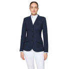 A woman modeling a navy blue equestrian-style blazer over a white collared shirt and white breeches, photographed against a light gray studio background.
