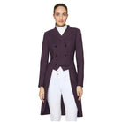 A woman modeling a dark plum double-breasted equestrian-style riding jacket over a white mock neck top and white riding pants, set against a solid light gray studio background.