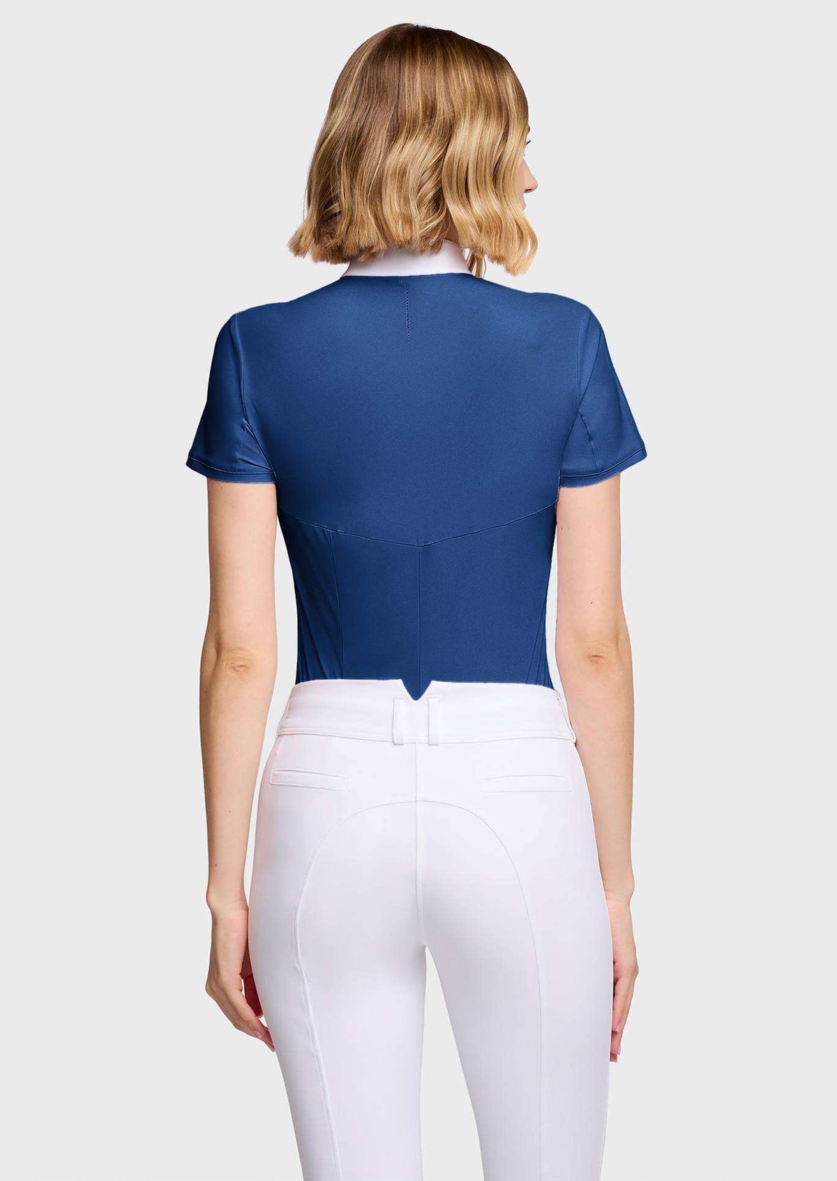 A woman shown from the back wearing a fitted short-sleeve royal blue cropped top and white riding breeches against a light gray studio background.