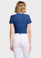 A woman shown from the back wearing a fitted short-sleeve royal blue cropped top and white riding breeches against a light gray studio background.