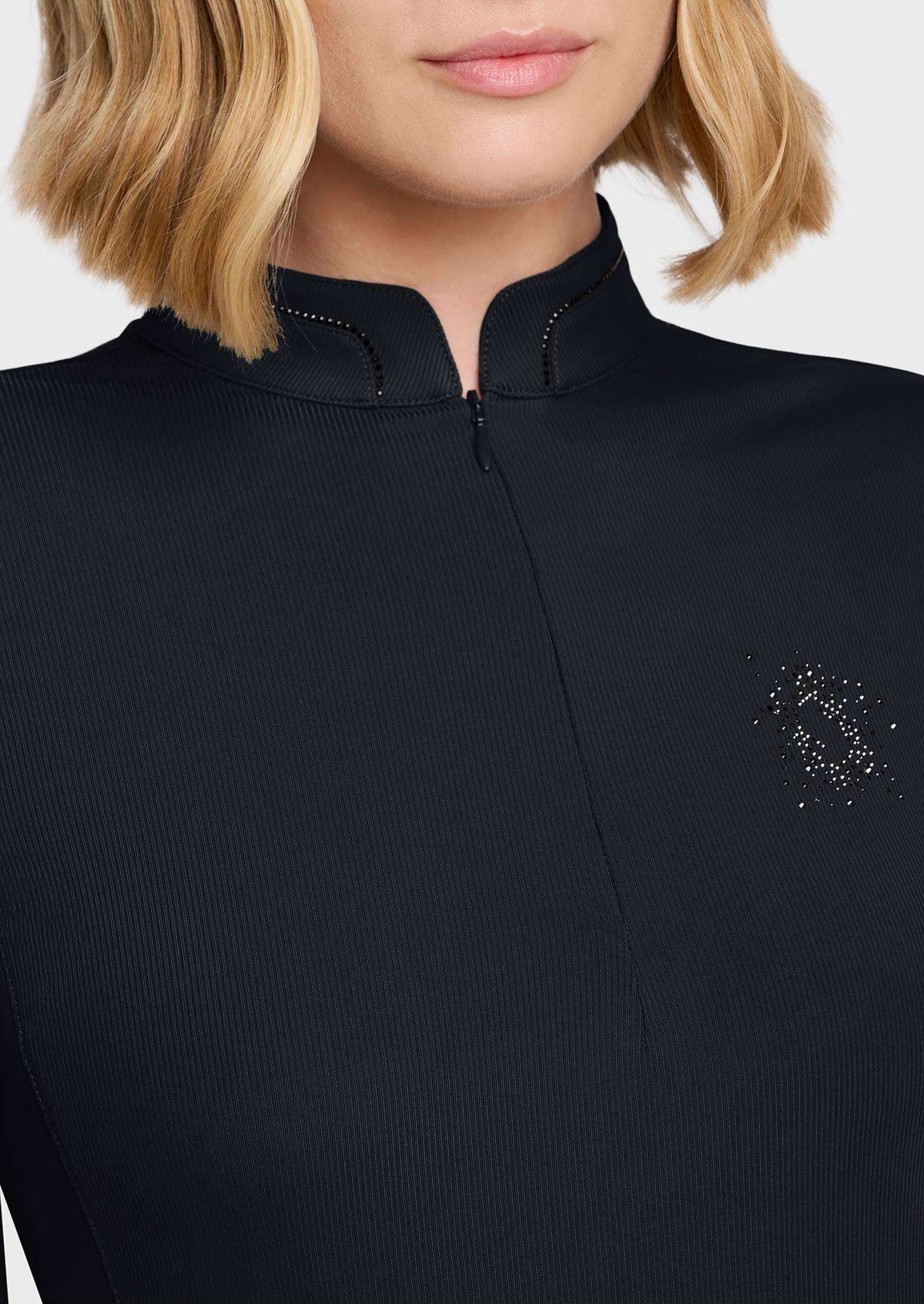 Close-up of a model wearing a black ribbed knit top with a mock neck, zipper, and a small rhinestone logo on the chest.