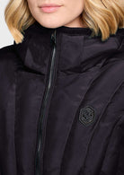 Close-up of a model wearing a black puffer jacket with a high collar, black zipper, and a small black hexagonal logo patch on the chest.