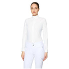 A woman modeling a white long-sleeve mock neck equestrian shirt and matching white riding pants against a light gray studio background.