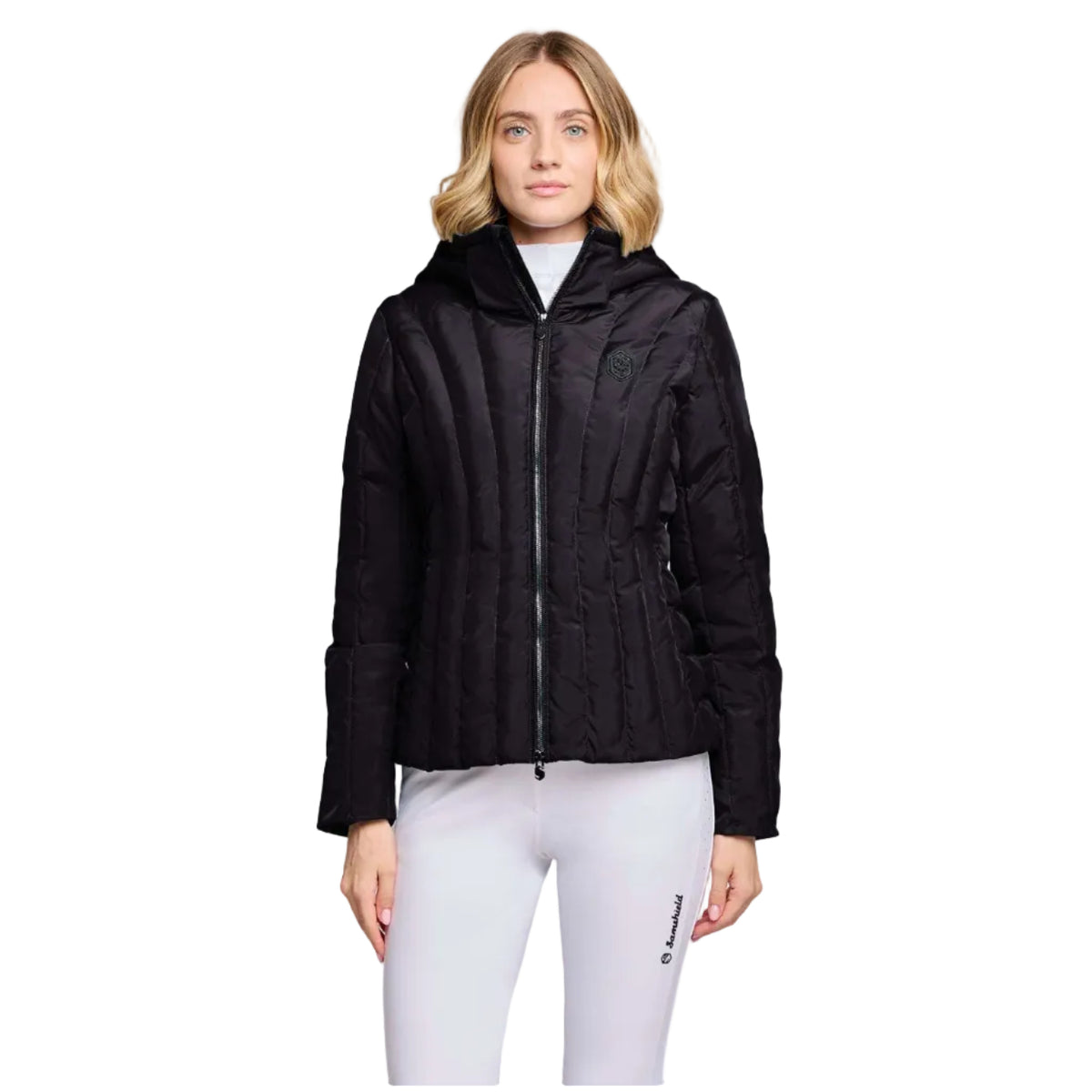 A woman modeling a black hooded quilted jacket with a front zipper, paired with white leggings, against a light gray studio background.