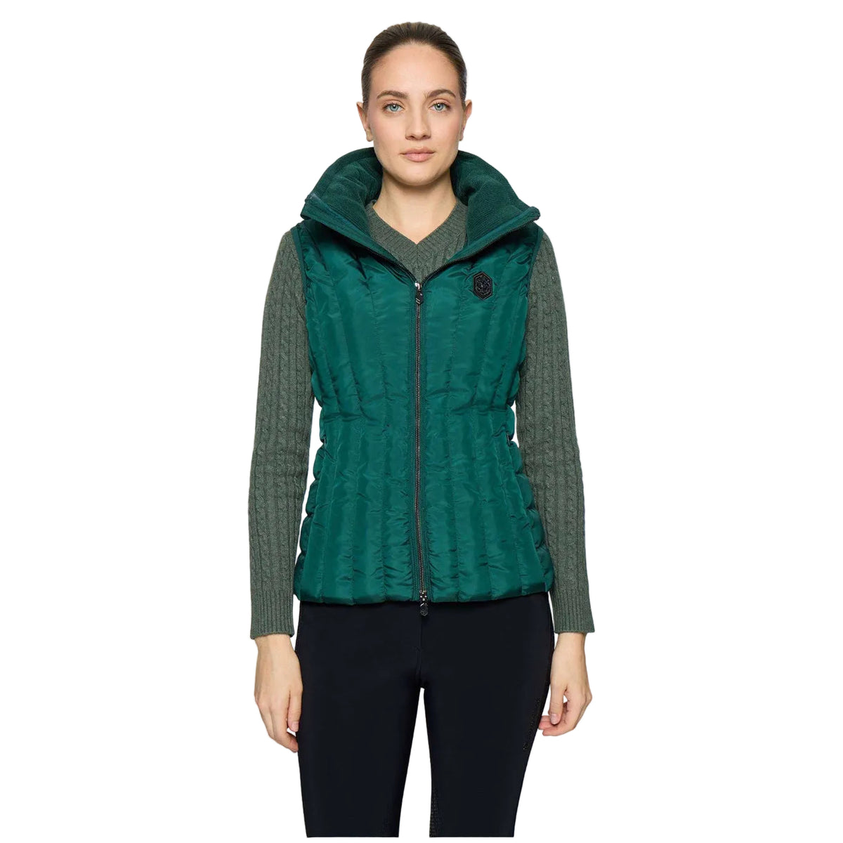 A woman modeling a dark green hooded puffer vest with ribbed knit sleeves, shown against a light gray studio background.