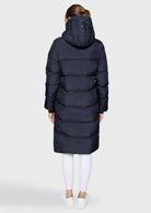 A woman viewed from the back wearing a long navy puffer coat with a hood, paired with white leggings and white sneakers, against a light gray studio background.