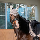 Woman in equestrian attire standing next to a horse in an indoor arena.