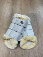 Pair of horse protective leg wraps with gray straps and beige fur on a wooden floor.