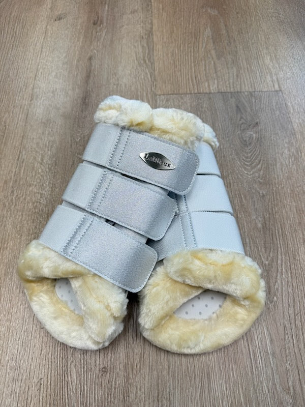 Pair of horse protective leg wraps with gray straps and beige fur on a wooden floor.