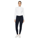 A woman modeling a white long-sleeve mock neck top and dark navy fitted pants with white sneakers, photographed against a light gray studio background.