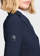 Close-up of a model wearing a navy blue structured blazer with decorative silver embellishments on the lapels and a matching navy sleeve patch, paired with a white collared shirt.