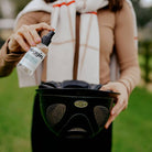 Person outdoors holding a spray bottle and black bag.