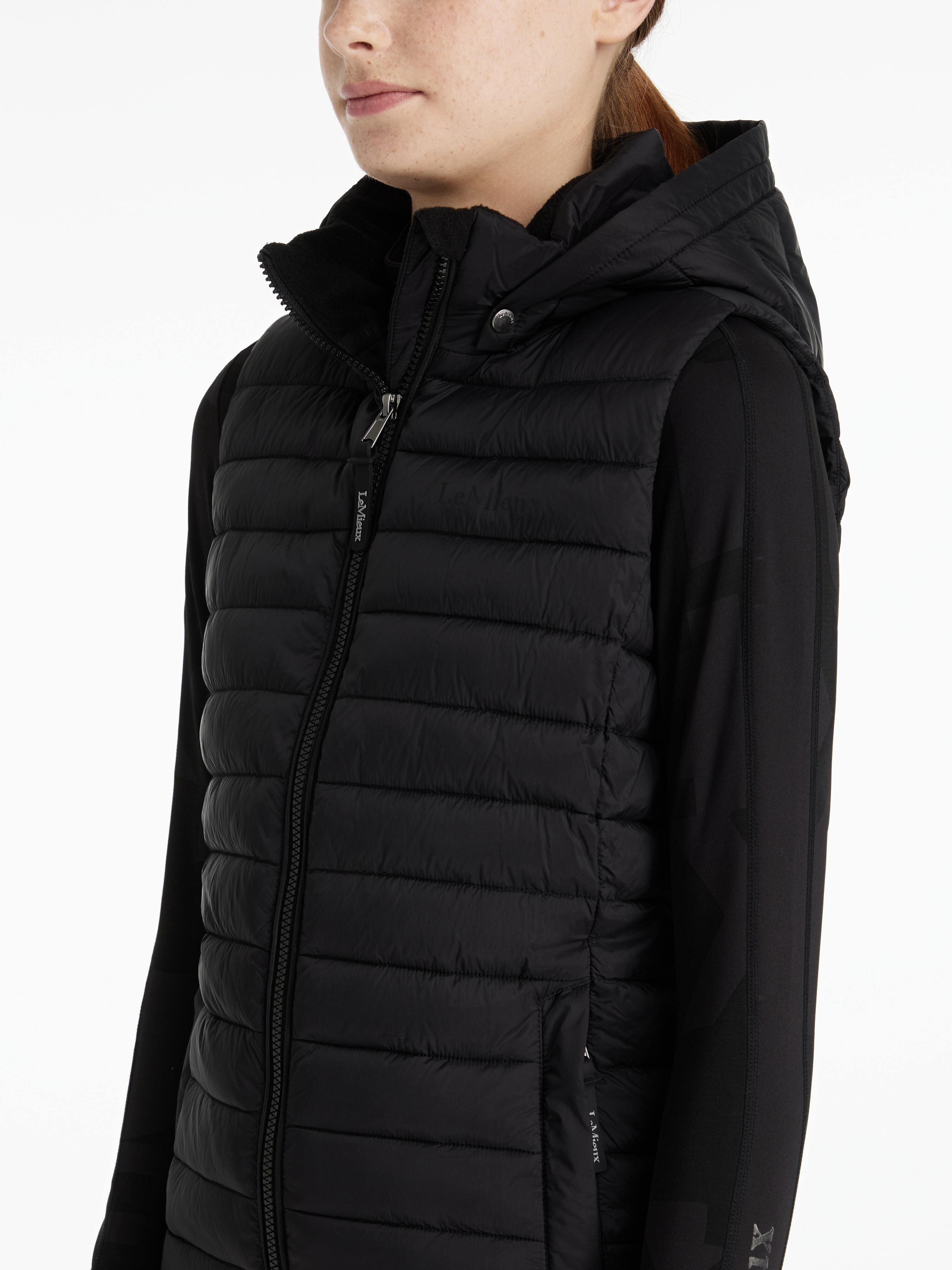 Person wearing a black puffer vest with a hood on a white background