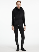 Woman wearing a black quilted jacket, black leggings, and black boots on a white background