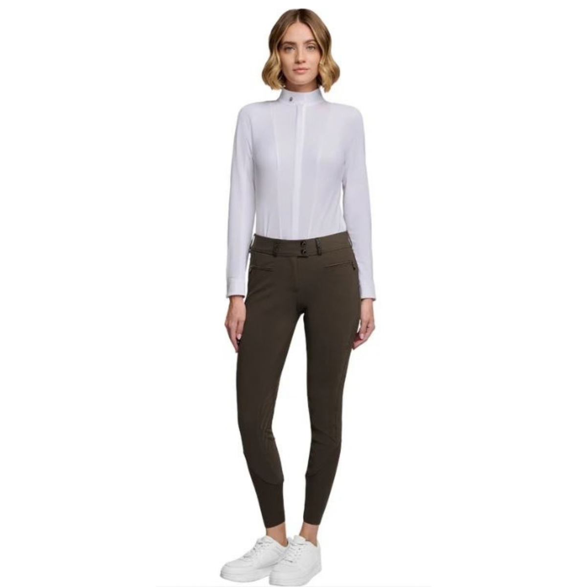A woman modeling a white long-sleeve mock-neck shirt paired with dark olive brown riding breeches and white sneakers, set against a plain white background.
